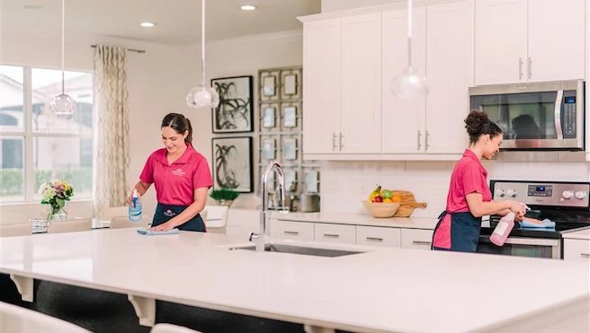 Two Molly Maid cleaning professionals wiping down a bright kitchen