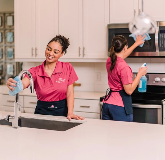 Molly Maid professionals wiping the counter and microwave in a white kitchen