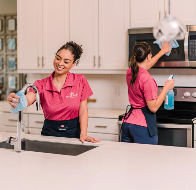 Cleaning professionals wiping the counter and microwave in a white kitchen